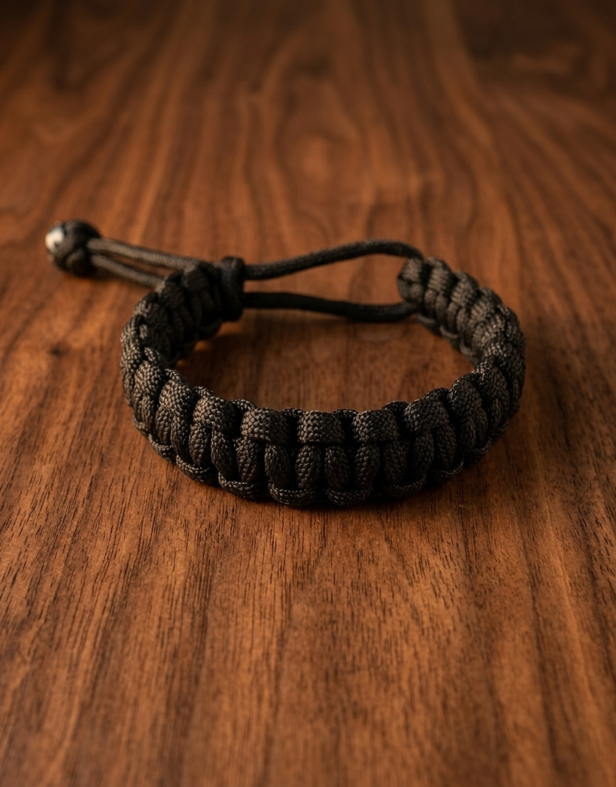 Black handmade paracord bracelet on a walnut table, a gift idea for him
