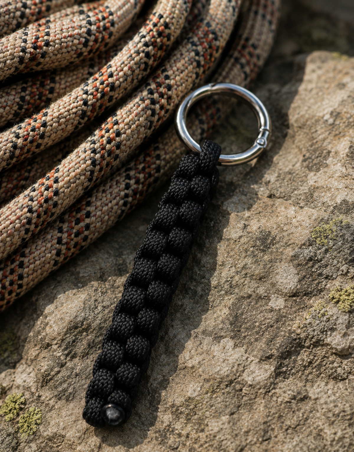 Saf black paracord keychain on a rock beside coiled rope