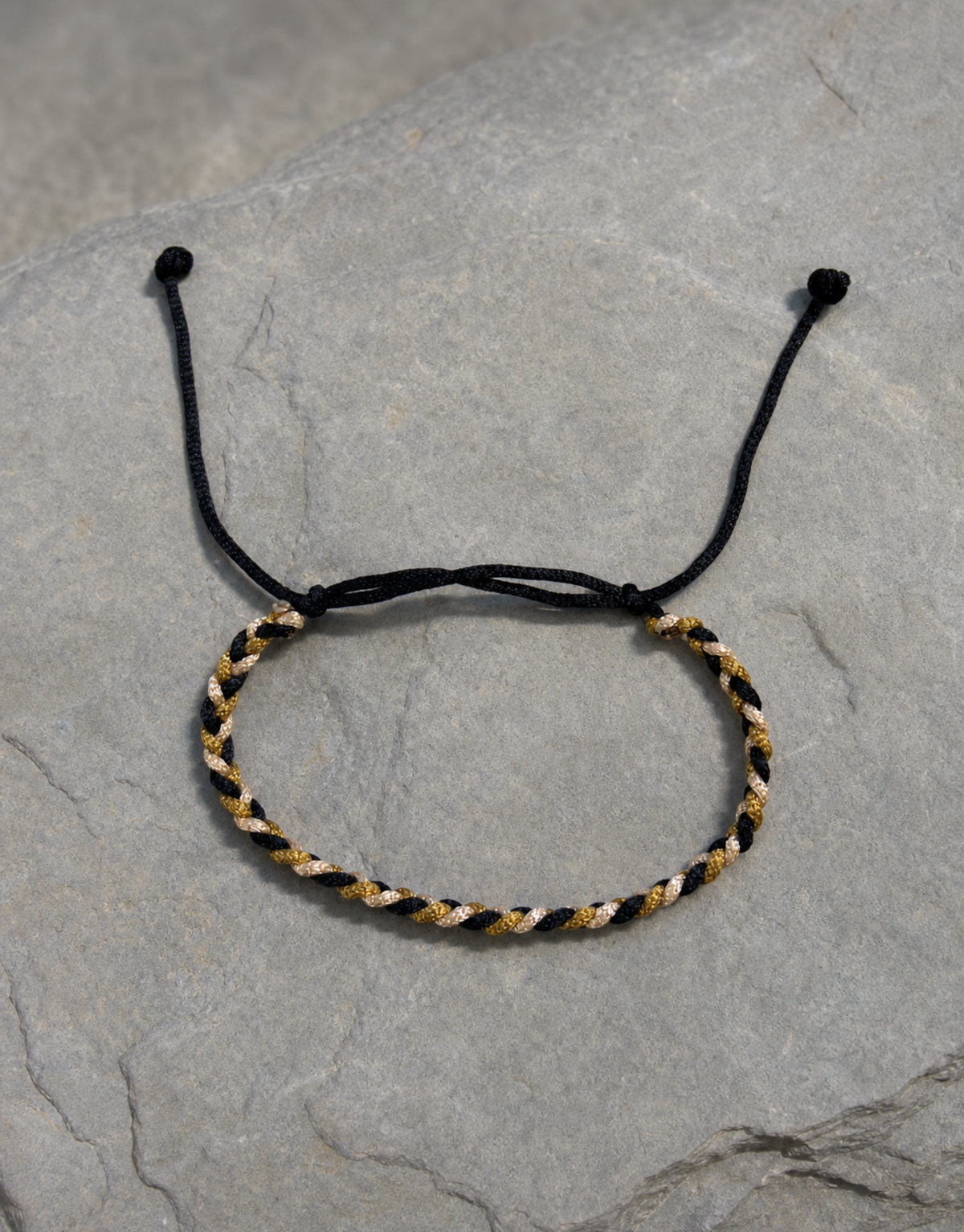 Zari black and gold braided bracelet on grey stone