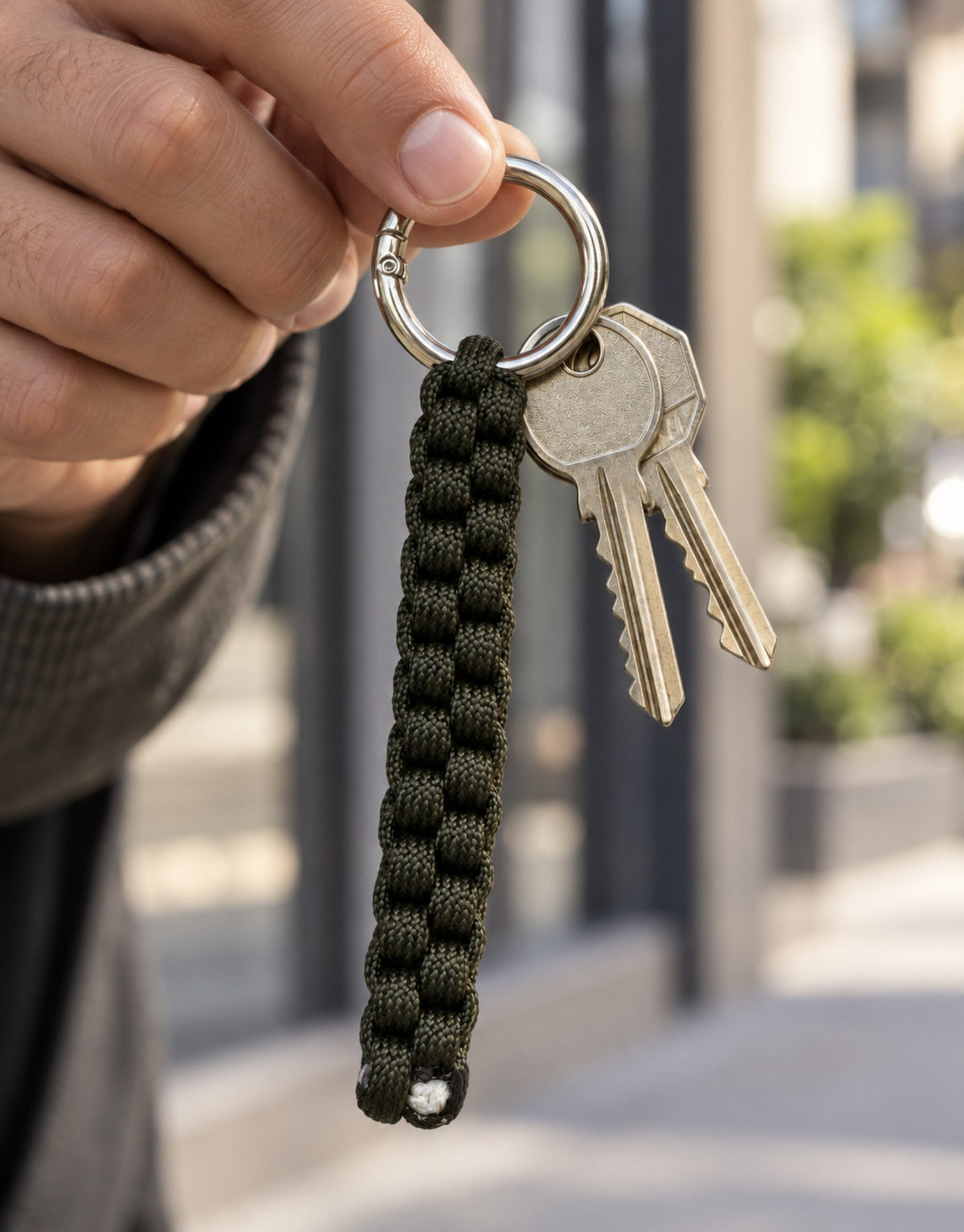 Hand holding the Saf dark green paracord keychain with keys